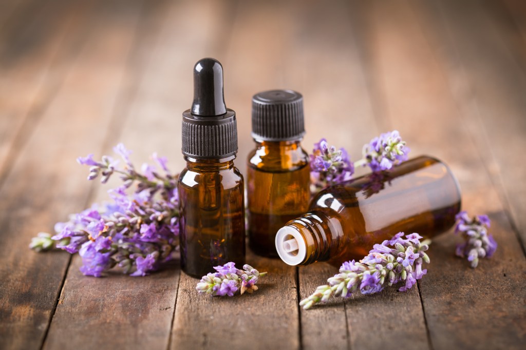 Three amber essential oil bottles sit on a wooden surface with sprigs of lavender.